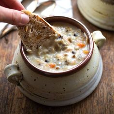 a hand holding a piece of bread over a bowl of soup