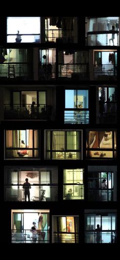 people are standing in the windows of an apartment building at night