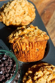 three muffins with chocolate chips in the middle on a black tray next to a bowl of oatmeal