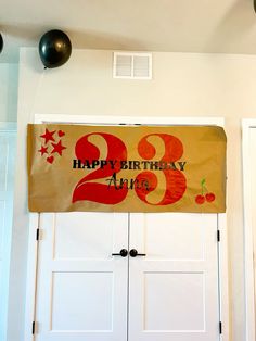 a happy birthday sign hanging from the ceiling in front of two white doors with balloons