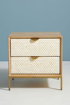 a white wicker dresser with two drawers on it's sides, against a blue wall