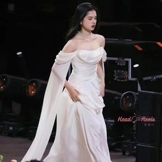 a woman in a white dress walking down a runway