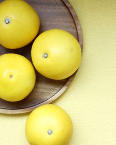 four lemons in a wooden bowl on a yellow surface