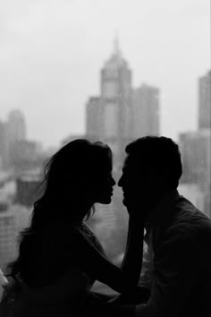 a man and woman standing next to each other in front of a window looking at each other