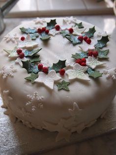 a white cake with holly and berries on top is sitting on a counter next to a knife