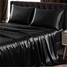 a bed with black sheets and pillows on top of it, next to a night stand