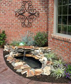 a small pond in the middle of a brick wall next to some plants and flowers