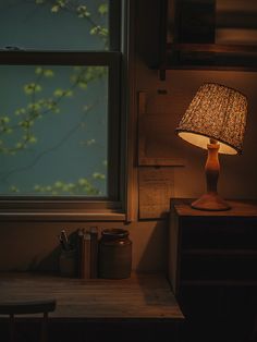 a lamp sitting on top of a wooden table next to a window with a green leafy tree outside