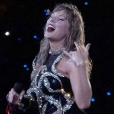 a woman singing into a microphone while wearing a black and white dress with gold trim