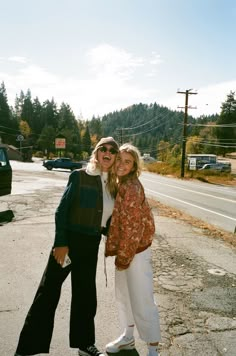 two women are standing on the side of the road posing for a photo with their arms around each other