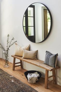 a wooden bench sitting under a round mirror