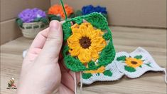 someone is holding up a crocheted sunflower ornament on a table