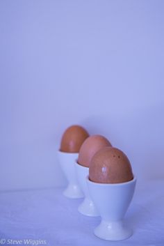 three brown eggs in white bowls on a white tablecloth with a light blue background