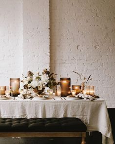 a table with candles and flowers on it in front of a white brick wall,