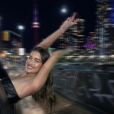 a woman is posing in the city at night with her arms up and legs spread out