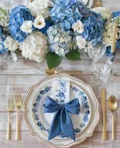 a table setting with blue and white flowers, silverware, and gold utensils