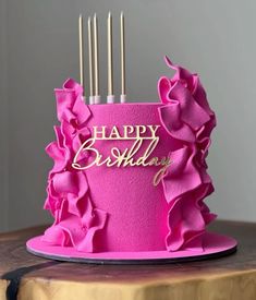 a pink birthday cake with gold lettering and ruffles on the top is sitting on a wooden table