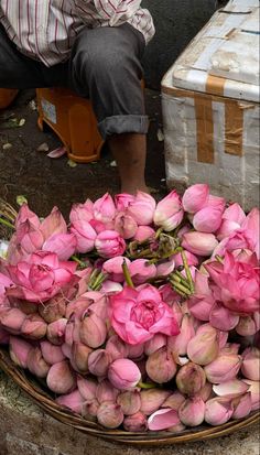 a basket full of pink flowers sitting next to a man on the ground in front of a box