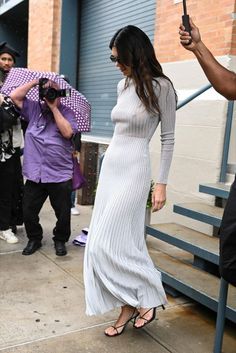 a woman in a long white dress is holding an umbrella and taking pictures with her cell phone