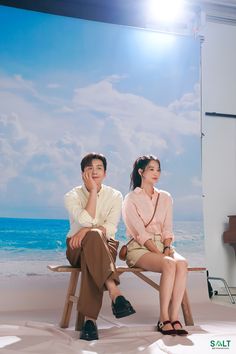 a man and woman sitting next to each other on a wooden bench near the ocean