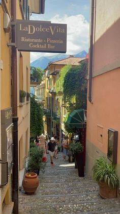 people are walking down the cobblestone street in an old town with shops and restaurants