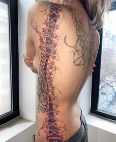 the back of a woman's body with tattoos on her stomach and arms, in front of a window