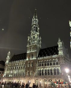 people are standing in front of a large building at night time with lights on it