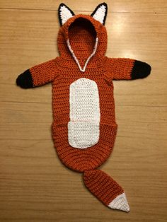 a crocheted fox costume laying on top of a wooden floor with it's hood up