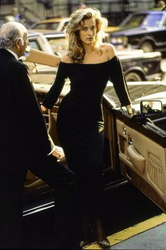 a woman in a black dress stepping out of a car with her hand on the door handle