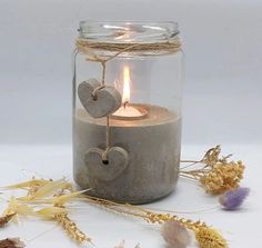 a glass jar filled with a candle and two hearts hanging from it's side