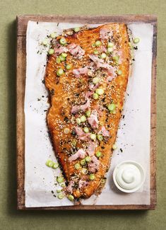 a piece of salmon on a wooden cutting board next to a small bowl of sauce