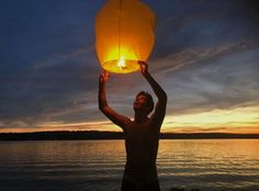 a man is holding up a lantern over the water