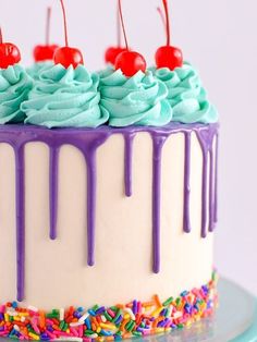 a cake with blue frosting and sprinkles on it, topped with cherries