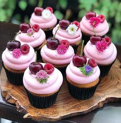 cupcakes with pink frosting, cherries and flowers on a wooden plate