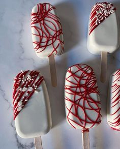 four white and red lollipops are sitting on a marble counter top, one is drizzled with icing