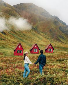 a man and woman holding hands in front of small red houses on the side of a mountain