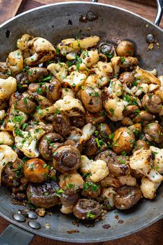 a skillet filled with mushrooms and other food on top of a wooden table next to utensils