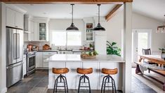 a kitchen with three stools in front of an island and two lights hanging from the ceiling