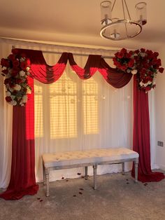 a white bench sitting in front of a window covered with red curtains and flowers on top of it