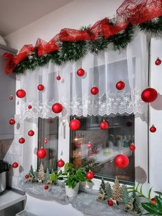 a window decorated for christmas with red balls and greenery hanging from the windowsill