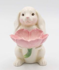 a white bunny holding a pink flower in its paws