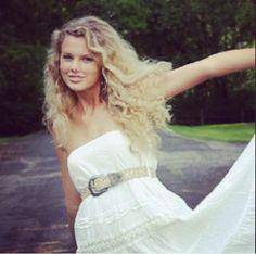 a beautiful blonde woman in a white dress posing for the camera with her arms outstretched