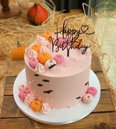 a birthday cake with pink frosting and pumpkins on the top is sitting on a wooden table