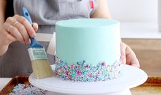 a woman is decorating a cake with sprinkles and a paintbrush