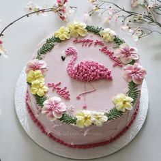 a cake decorated with flowers and a pink flamingo on it's side sitting on a table