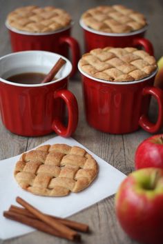 apples, cinnamon sticks and two red mugs on a table