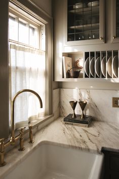 a kitchen sink sitting under a window next to a white counter top with gold faucets