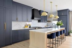 a kitchen with blue cabinets and gold pendant lights hanging from the ceiling, along with bar stools