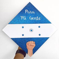 a hand holding a blue graduation cap that says para mi gente with stars on it