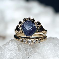 a gold ring with a blue stone surrounded by black and white diamonds on top of a rock